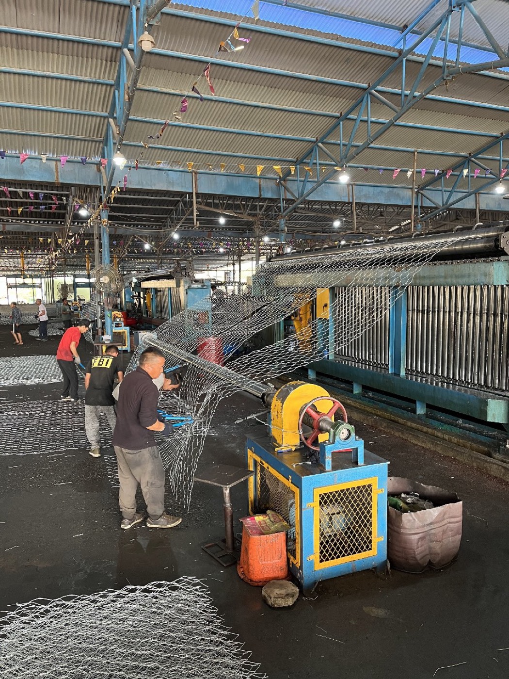 Workers operating a wire-mesh weaving machine on the factory floor